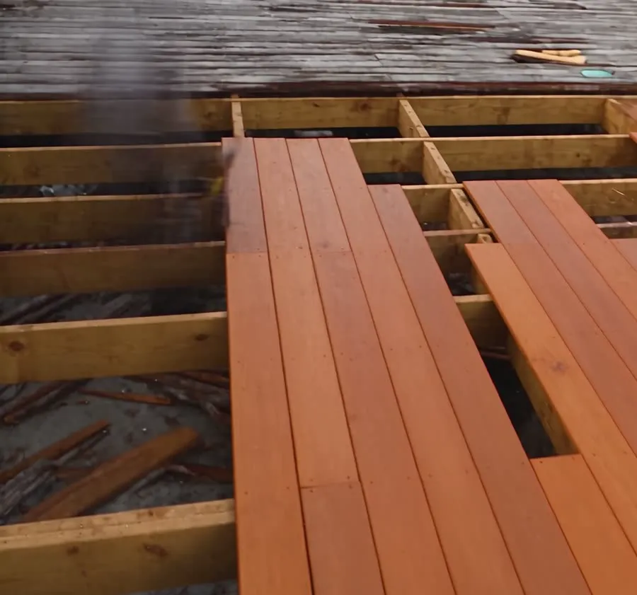 Old gray deck boards next to new boards on a deck frame